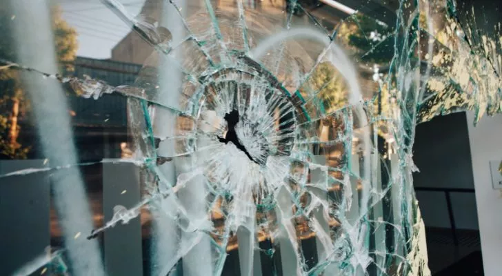 A glass window with a large hole in it and shattered glass around the hole
