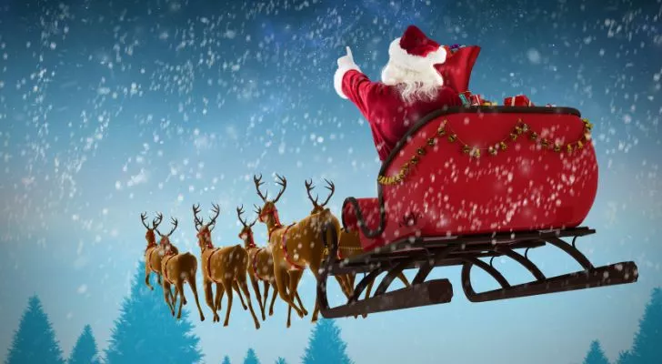 Santa rides his sleigh through a snowy sky led by flying reindeer