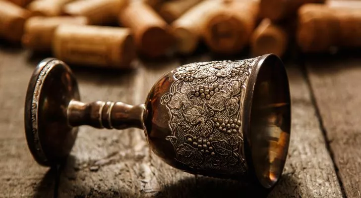A medieval-style wine goblet lays on its side on a table surrounded by corks