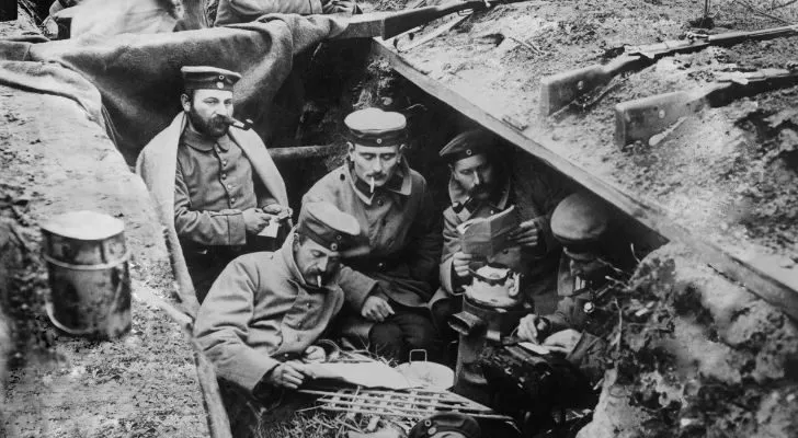 Some men in a trench pass the time by smoking and reading