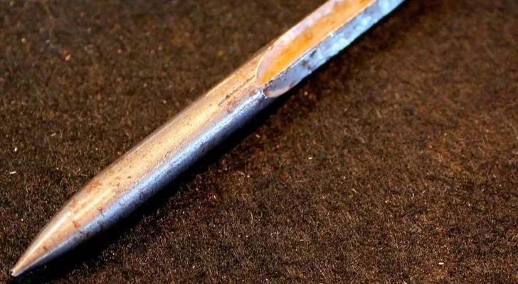 A thick metal dart with a point at one end and tapering into a cross at the other