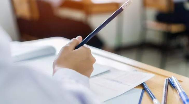 A man's hand holds a pencil as he answers a test