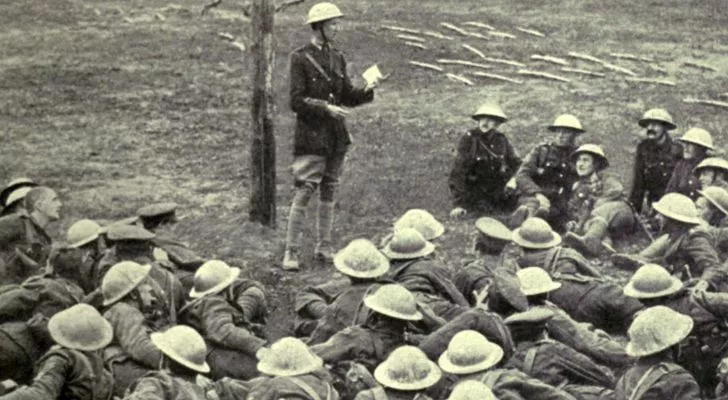 A group of Allied soldiers lie on the ground and receive instructions from a superior officer