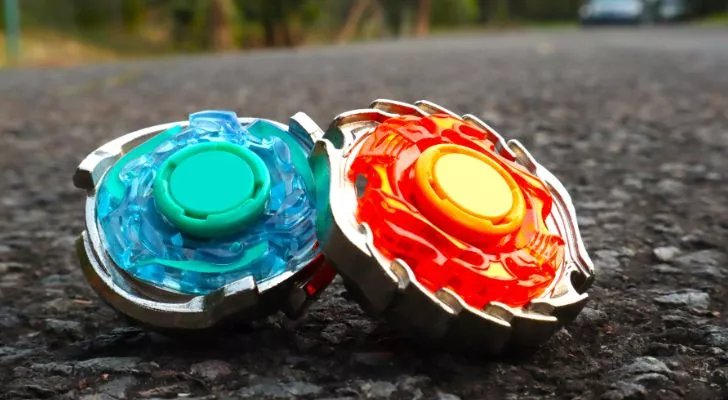 A red Beyblade leans against a blue one in the middle of a road