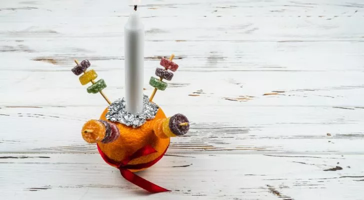An orange wrapped in a red ribbon with a candle placed on top and assorted sweets attached with cocktail sticks