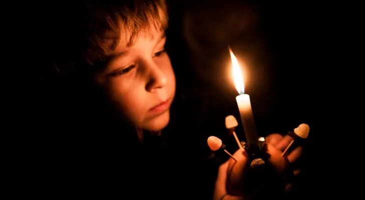 A child holds a lit Christingle up to their face in the dark