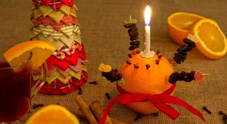 A Christingle next to assorted festive items including cut oranges and mulled wine