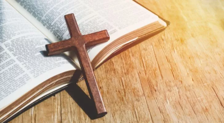 A small wooden cross leans on an open Bible