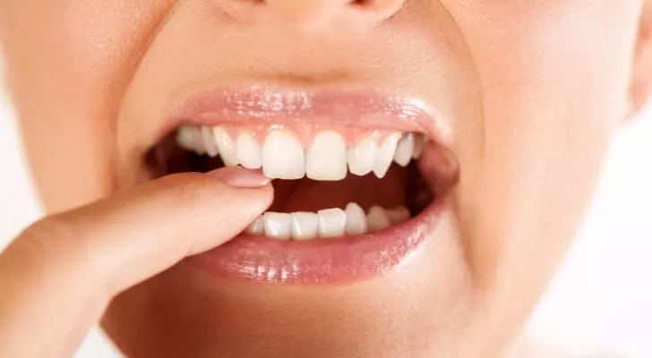 A woman puts a finger between her teeth and holds it there with her teeth