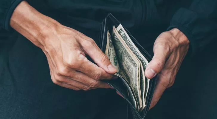 A man opens a wallet to find only a small amount of cash in it