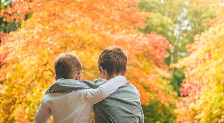 Two young boys with their arms around each other in front of a tree in Autumn