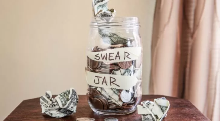 A glass jar labelled "swear jar" is full of coins and crumpled dollar bills