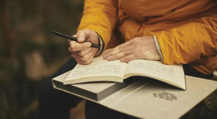 Someone holding a pen writes notes in a notebook