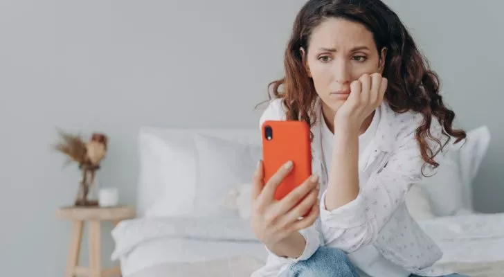 A woman sits and stares at her phone in a depressed manner
