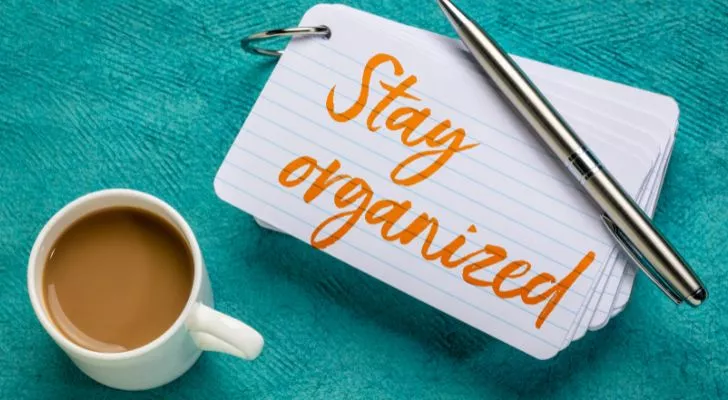 A note with the words "stay organized" written on it next to a cup of coffee and a pen