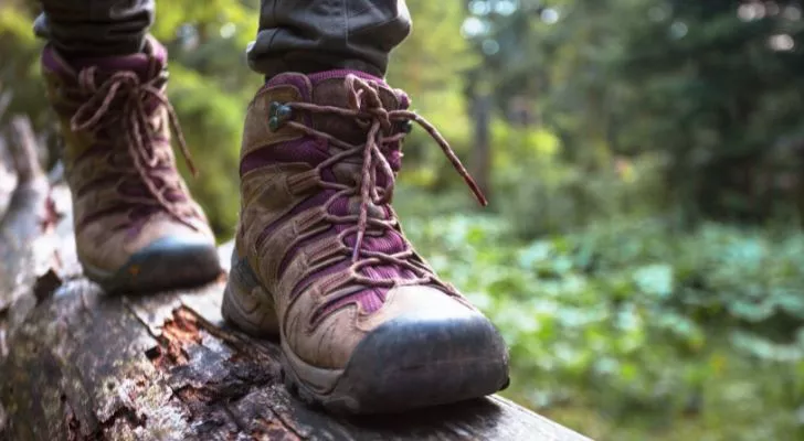 A person in hiking boots walks along a log in a forest