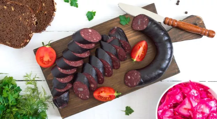 A dark sausage is sliced and served on a chopping board