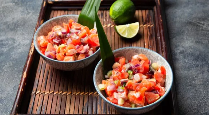 Two bowls of diced tomatoes and salmon on a tray with limes