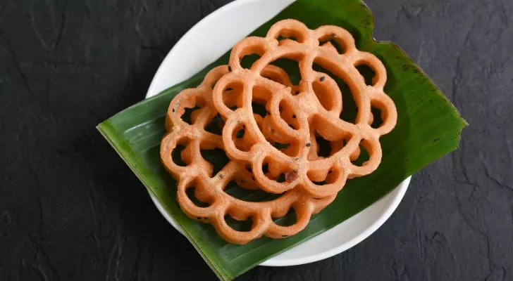 Intricate achappam pastries sit on a large leaf on a plate
