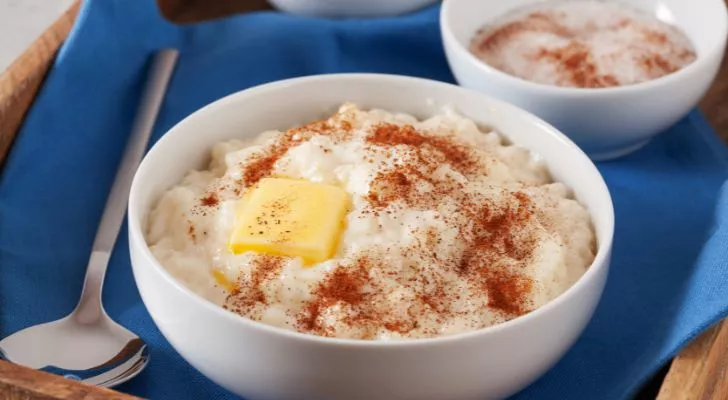 A bowl of rice pudding with a slice of butter and sprinkling of cinnamon