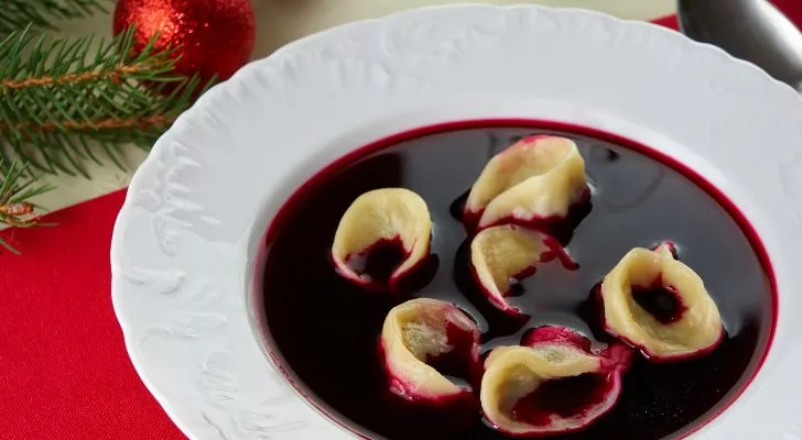 A bowl of deep red colored soup with dumplings floating in it