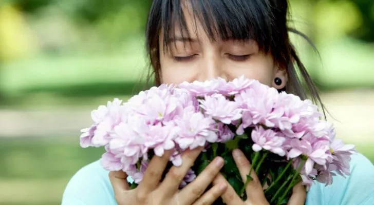 A woman smelling a boquet of light-purple flowers