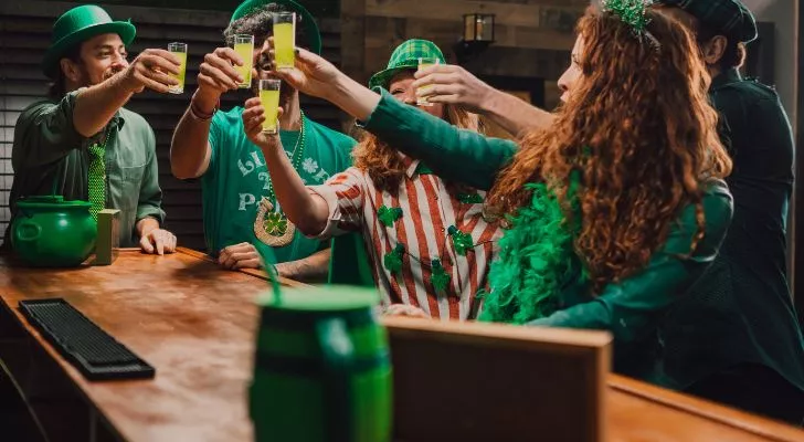 4 friends wearing green clothing cheers a green drink in a bar