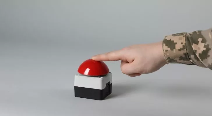 Someone in military uniform putting their finger on a large red button