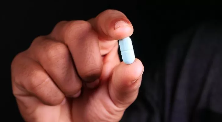 A person's hand holding a bright blue pill