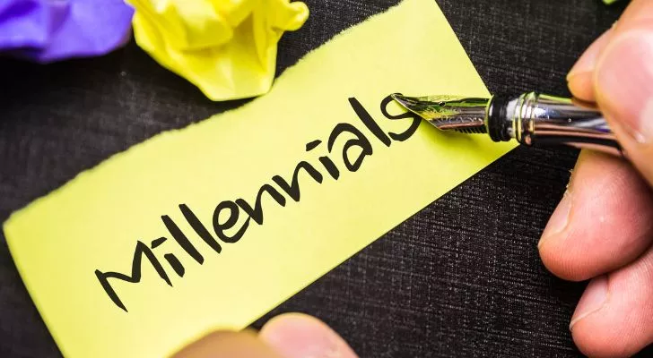 A person writing the word "Millennials" on a yellow piece of paper