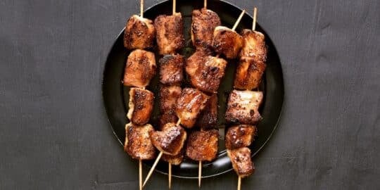 Grilled meat skewers arranged on a black plate