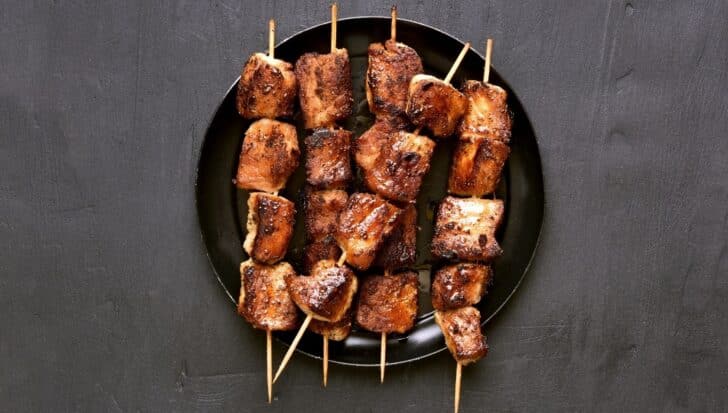 Grilled meat skewers arranged on a black plate