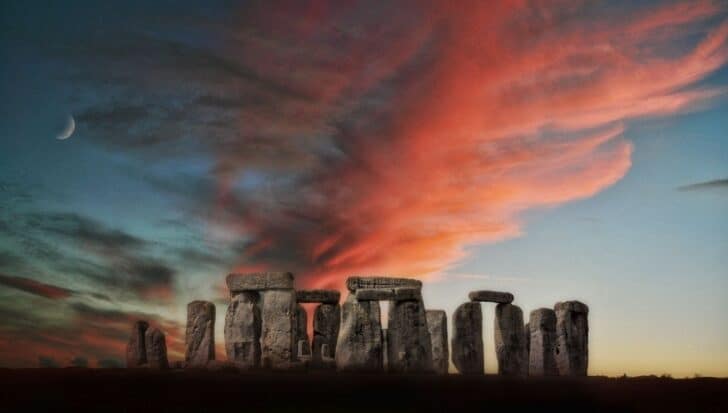 Stonehenge with a dramatic sunset sky and a crescent moon