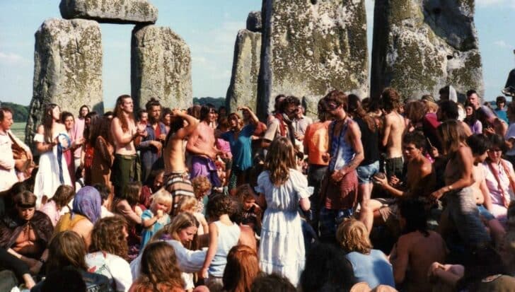 A large group of people gathered at Stonehenge enjoying a festival, with attendees dressed in casual and colorful clothing around the iconic stone structure