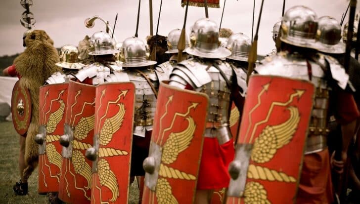Row of Roman soldiers with helmets and red shields featuring gold designs, emphasizing the frequent visits of Romans to Stonehenge