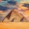 The Pyramids of Giza under a colorful sunset sky with a sandy foreground