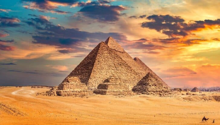 The Pyramids of Giza under a colorful sunset sky with a sandy foreground