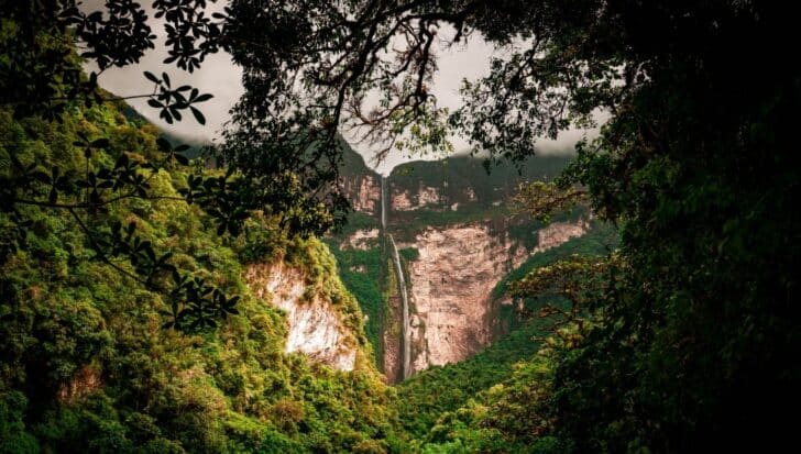 Lush green rainforest surrounding a tall waterfall cascading down a steep cliff, highlighting Peru's diverse climate