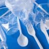 Assorted plastic items, including bottles, cups, a plastic bag, a fork, and a spoon, arranged on a blue background