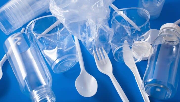 Assorted plastic items, including bottles, cups, a plastic bag, a fork, and a spoon, arranged on a blue background