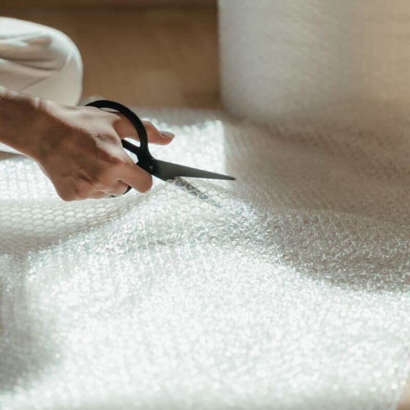 A person cutting a sheet of bubble wrap with scissors on a wooden surface