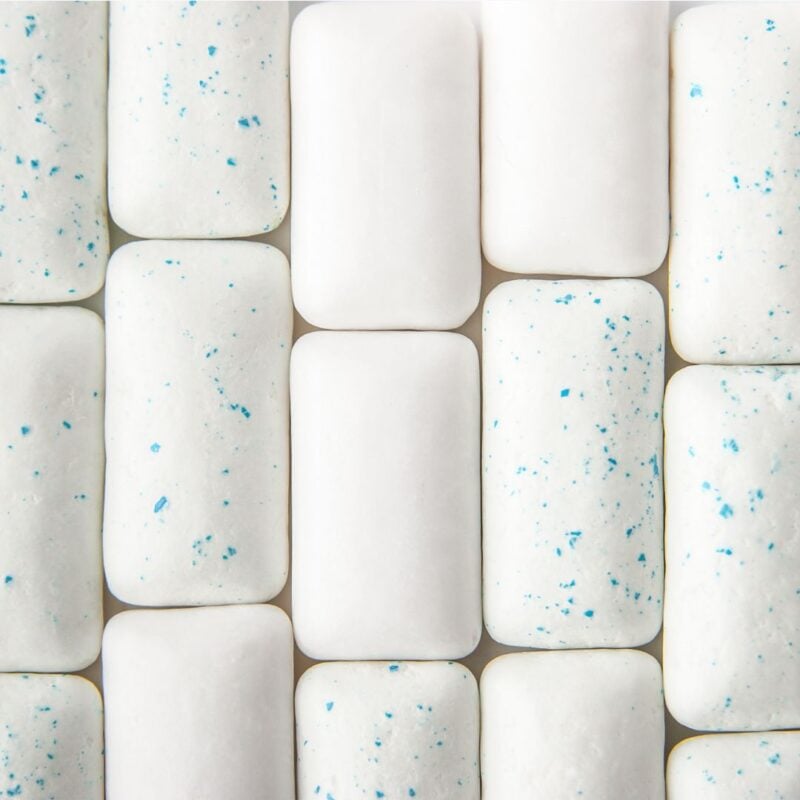 Close-up view of several rectangular white chewing gum pieces, some with blue speckles
