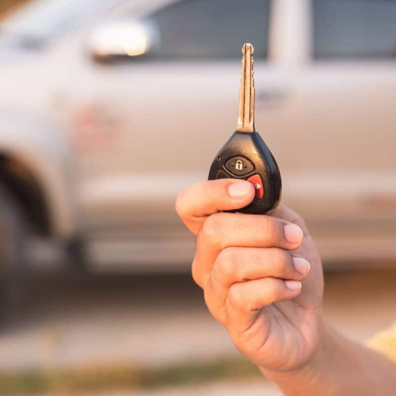 A hand holding a car key with a vehicle in the background