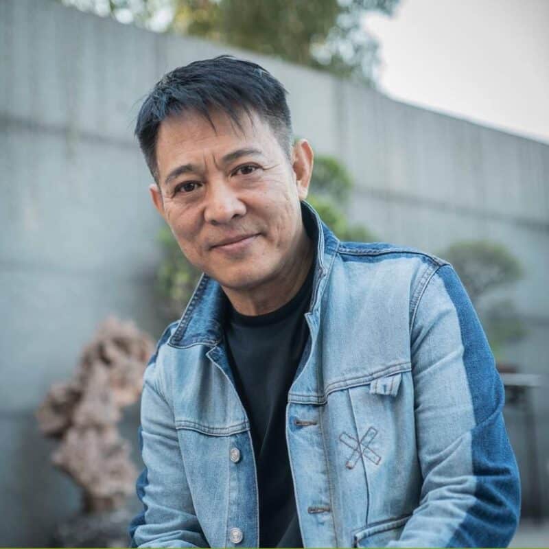 Jet Li smiling, outdoors, wearing a denim jacket