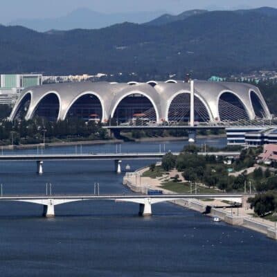 Rungrado 1st of May Stadium with distinctive arches located next to a river, surrounded by bridges