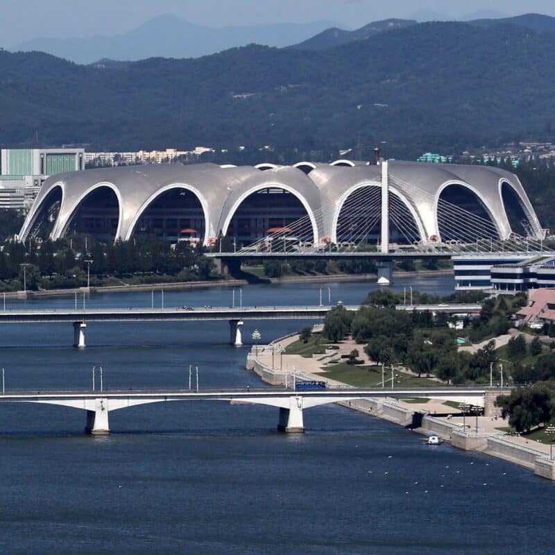 Rungrado 1st of May Stadium with distinctive arches located next to a river, surrounded by bridges