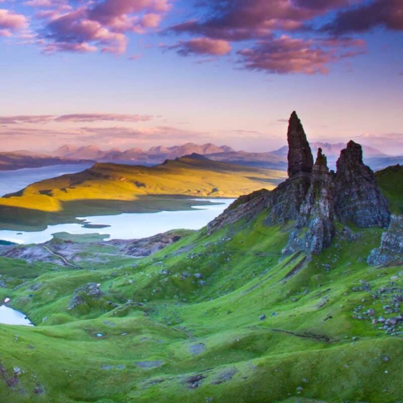 Scenic landscape of the Old Man of Storr on the Isle of Skye with green hills and rock formations under a colorful sky