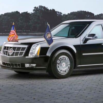 Presidential car with American flags on the front, black in color, parked on a cobblestone surface