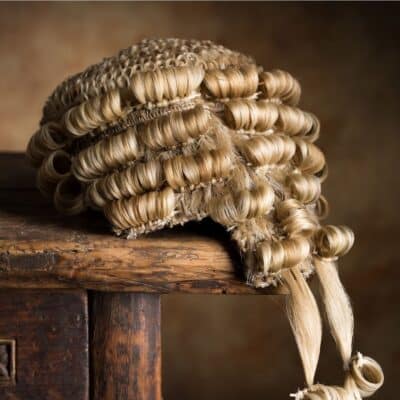 A traditional British powdered wig with tight curls resting on a wooden surface
