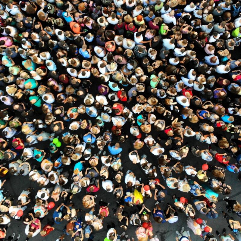 A large crowd of people seen from above, showcasing diverse clothing and hairstyles, densely packed together